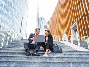 Zwei Menschen sitzen auf einer Treppe im Finanzzentrum und betrachten einen Bildschirm